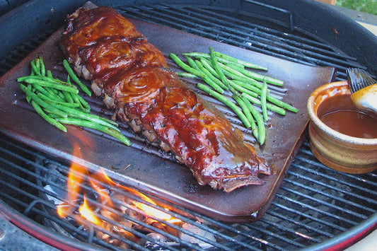 Ribs and green beans on a grill with a side of sauce.