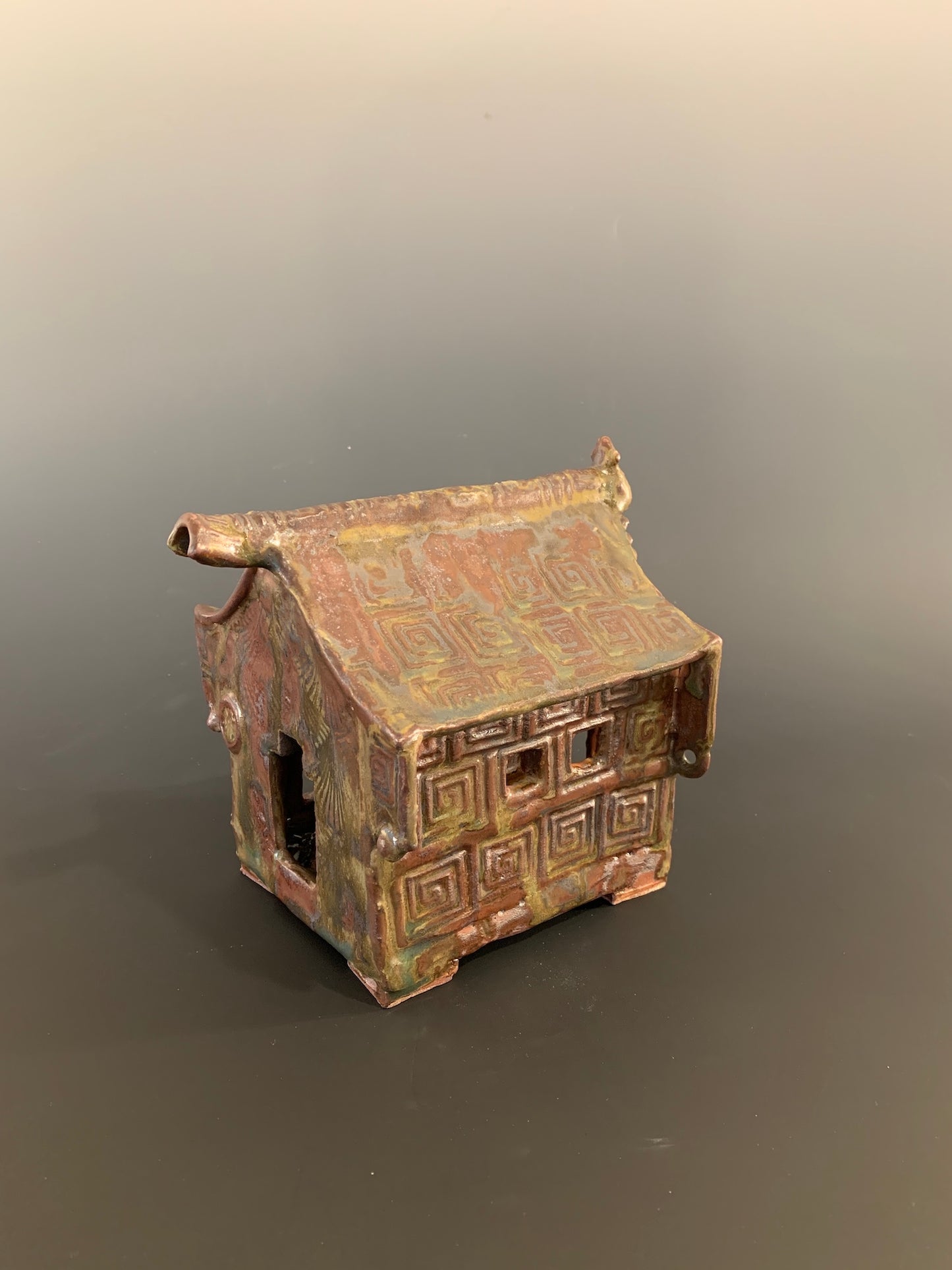 Small ceramic model of a house with geometric patterns on a gray background