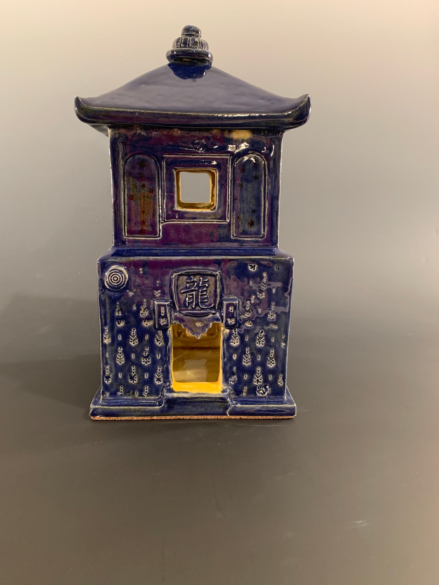 Blue ceramic house with intricate designs on a gray background