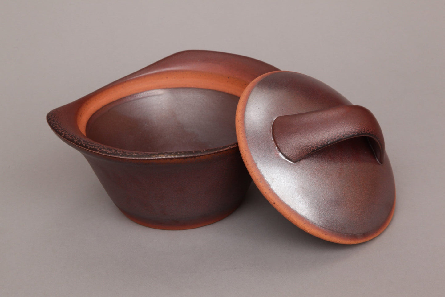 Flameware clay casserole pot in bordeaux color with lid off.