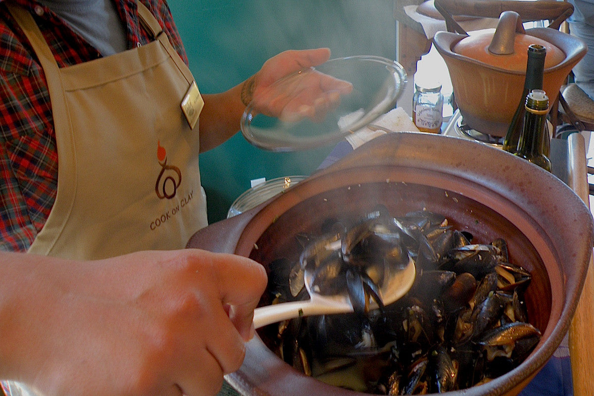 Person cooking mussels in a pot with steam rising, wearing an apron.