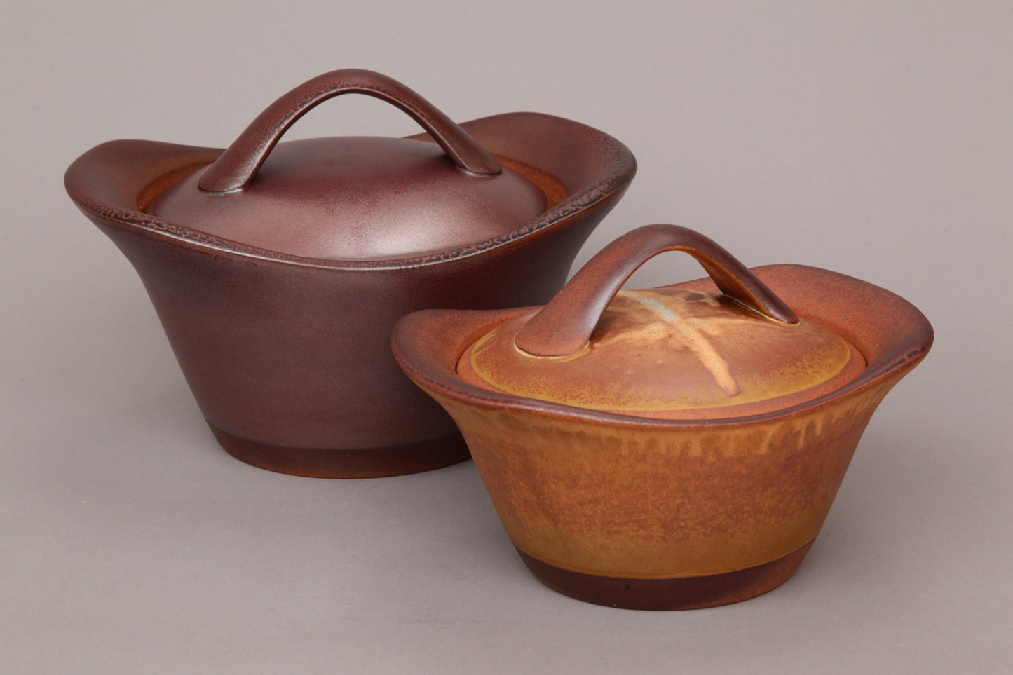 Two ceramic pots with lids on a plain background
