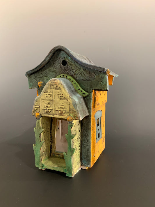 Decorative ceramic house with green and orange colors on a gray background