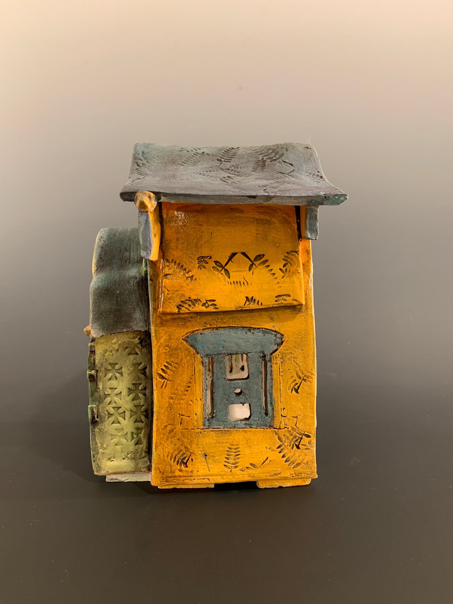 Decorative ceramic house with green and orange colors on a gray background
