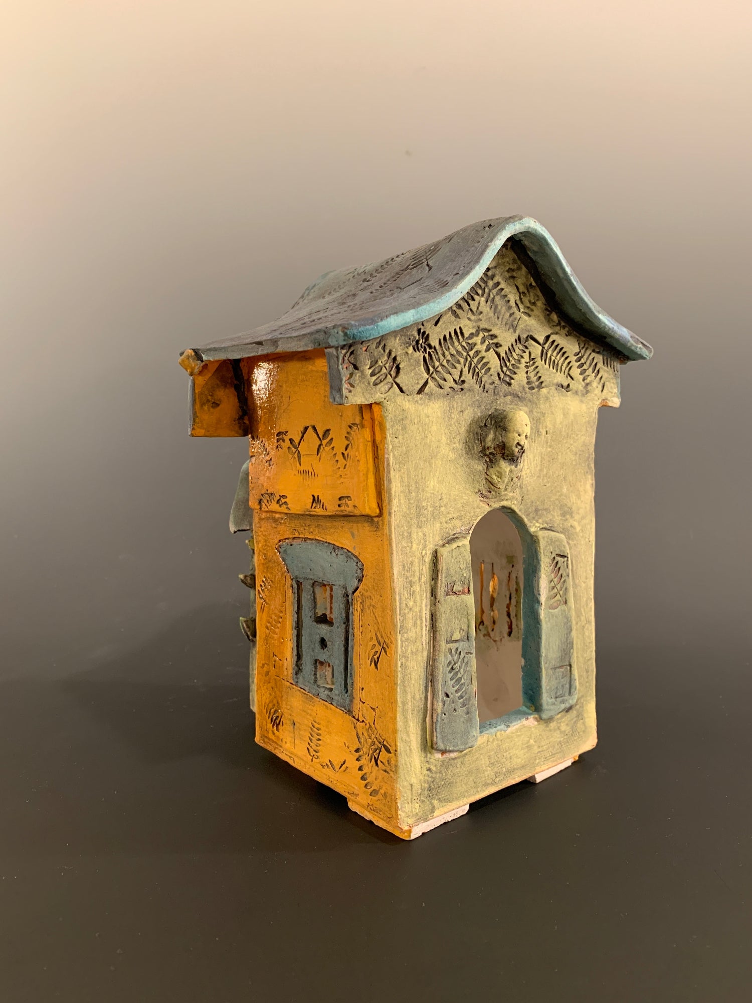Decorative ceramic house with green and orange colors on a gray background