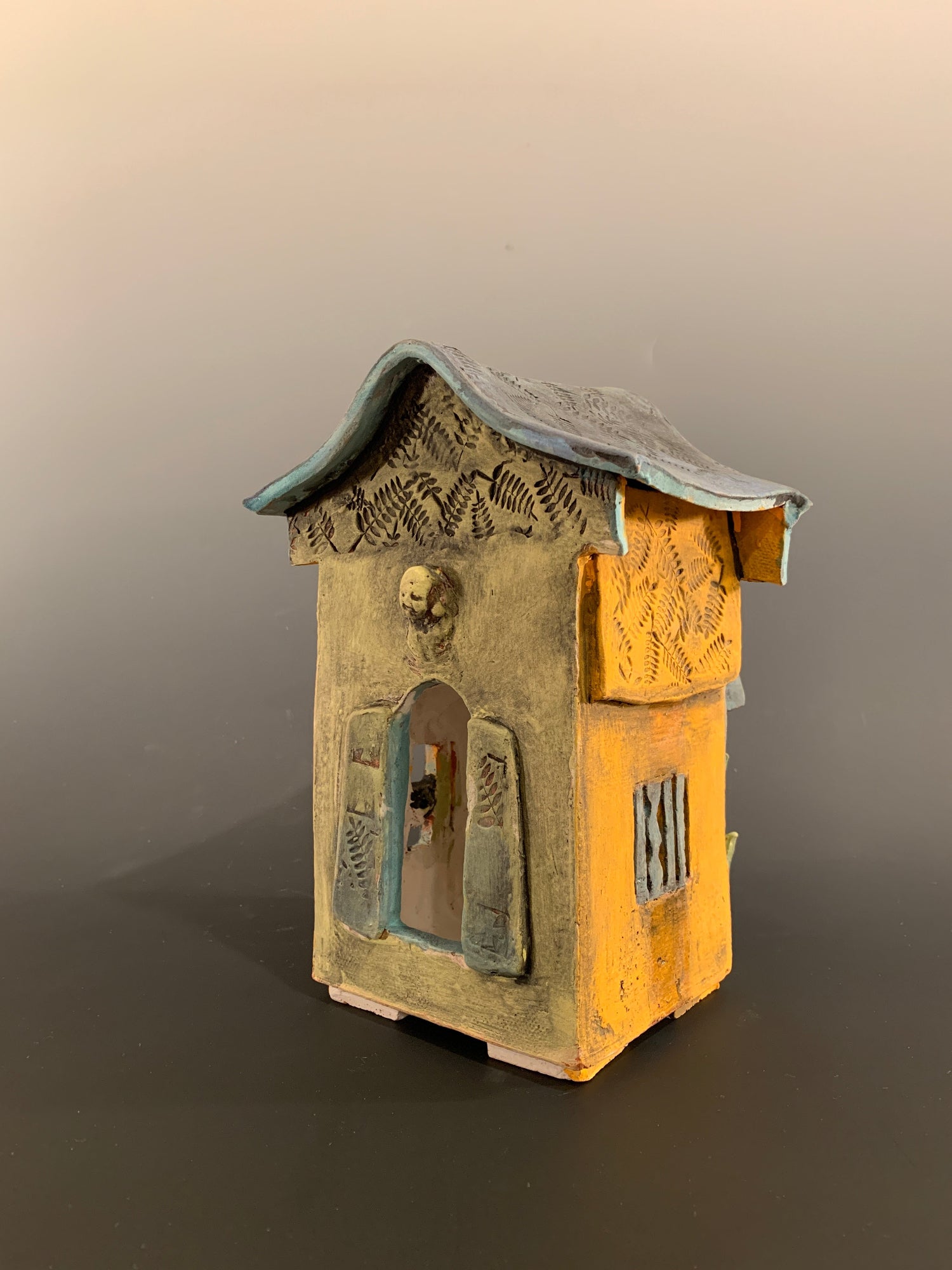 Decorative ceramic house with green and orange colors on a gray background