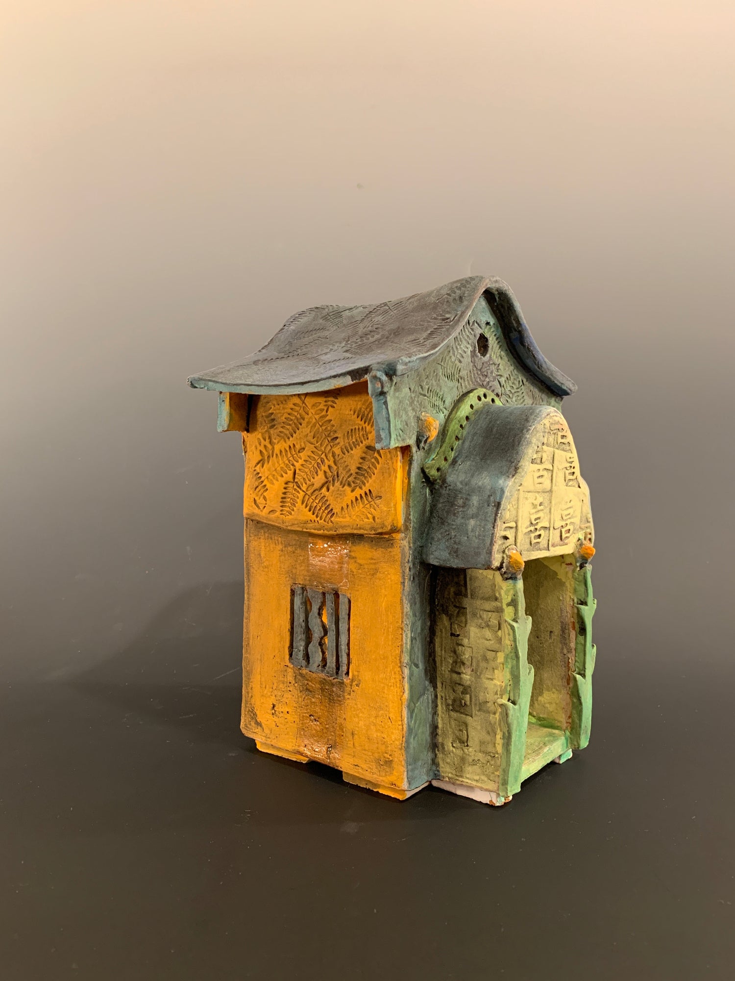 Decorative ceramic house with green and orange colors on a gray background