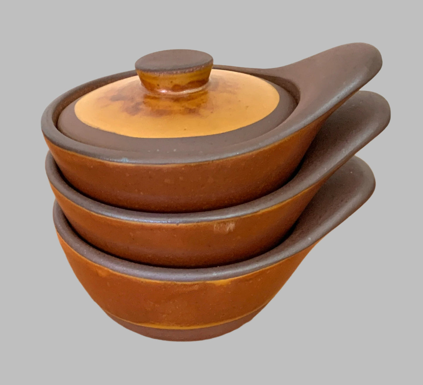 Stack of brown ceramic pots with lids on a gray background