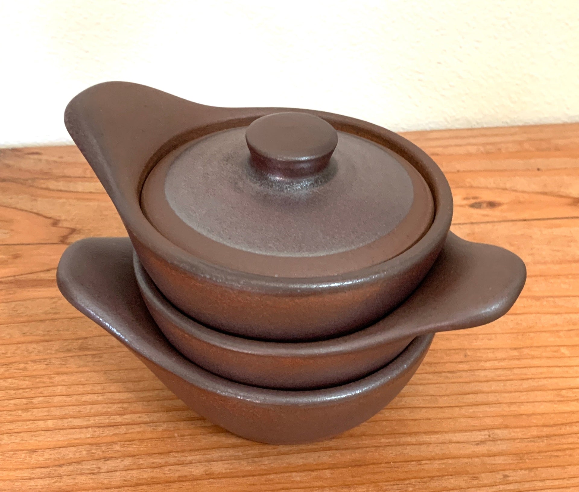 Stack of brown ceramic pots with lids on a wooden surface