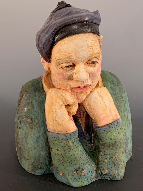 Vintage ceramic sculpture of a person with a dark hat and green clothing on a gray background