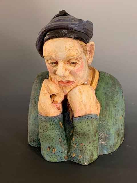 Vintage ceramic sculpture of a person with a dark hat and green clothing on a gray background