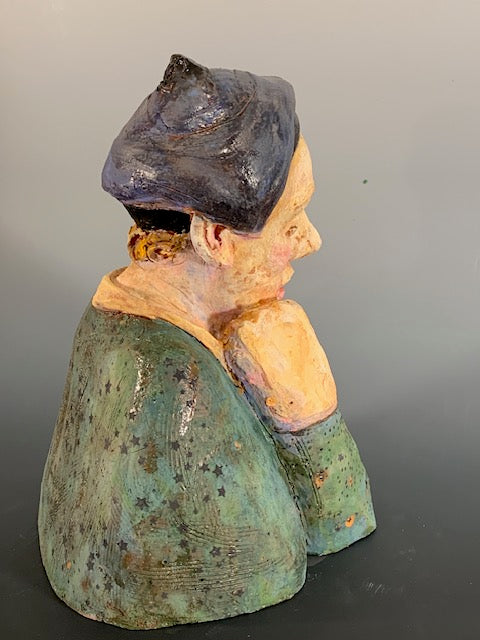 Vintage ceramic sculpture of a person with a dark hat and green clothing on a gray background