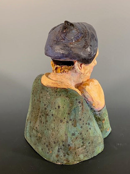 Vintage ceramic sculpture of a person with a dark hat and green clothing on a gray background