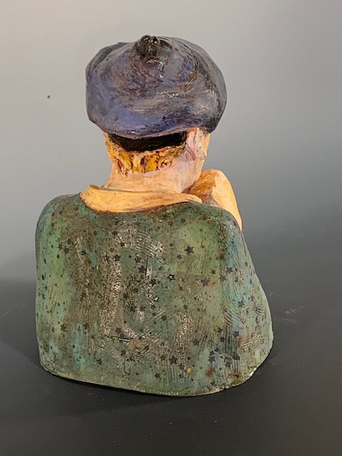 Vintage ceramic sculpture of a person with a dark hat and green clothing on a gray background