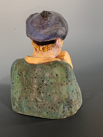 Vintage ceramic sculpture of a person with a dark hat and green clothing on a gray background