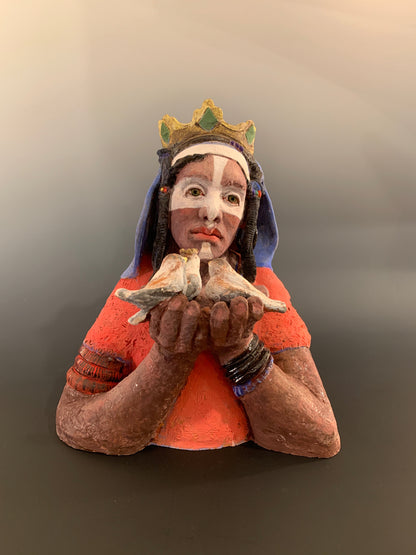 Traditional figurine with a colorful headdress and holding birds against a plain background