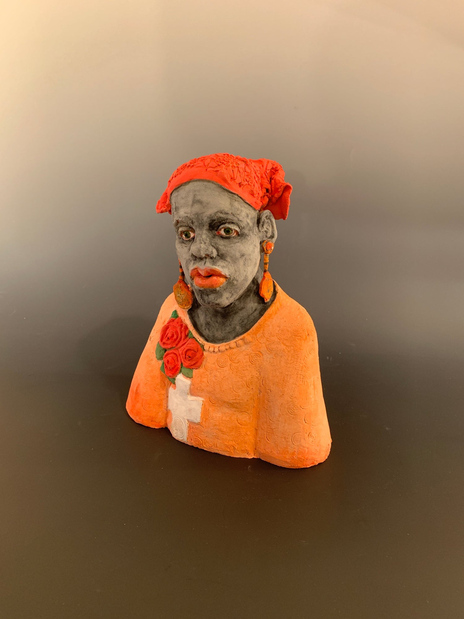 Small figurine of a person wearing an orange hood with floral details on a plain background
