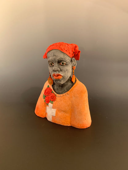 Small figurine of a person wearing an orange hood with floral details on a plain background
