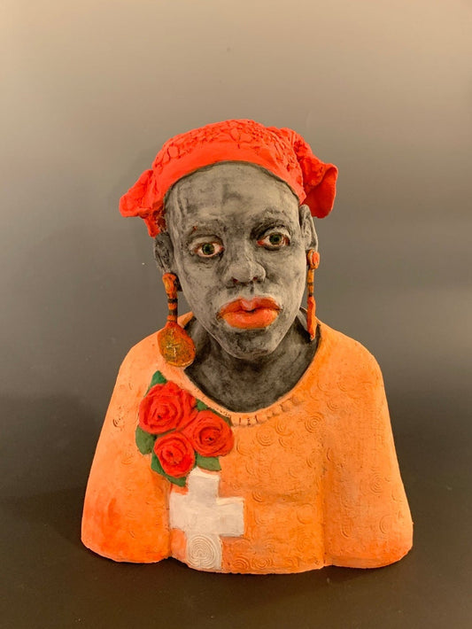 Small figurine of a person wearing an orange hood with floral details on a plain background
