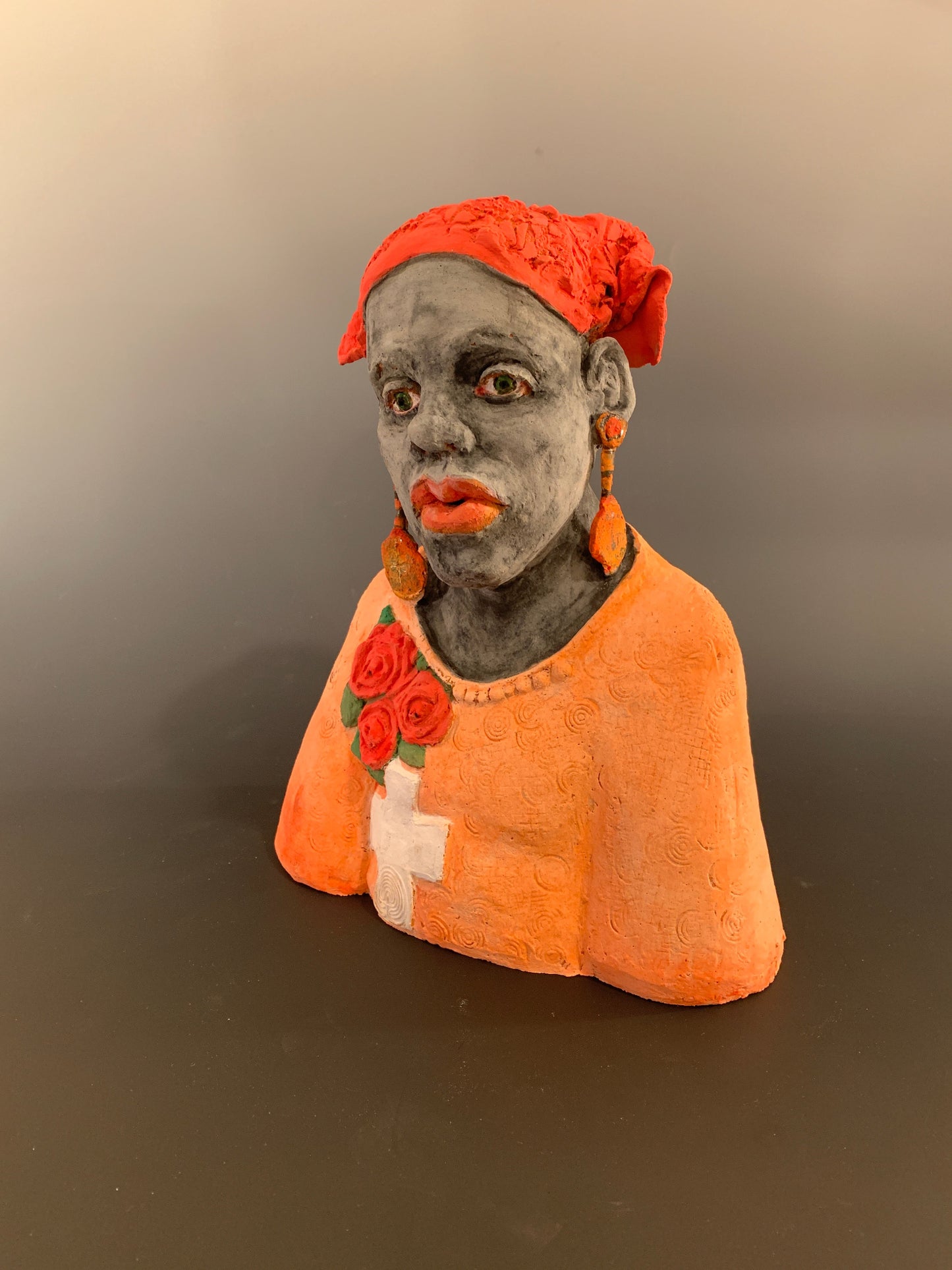 Small figurine of a person wearing an orange hood with floral details on a plain background