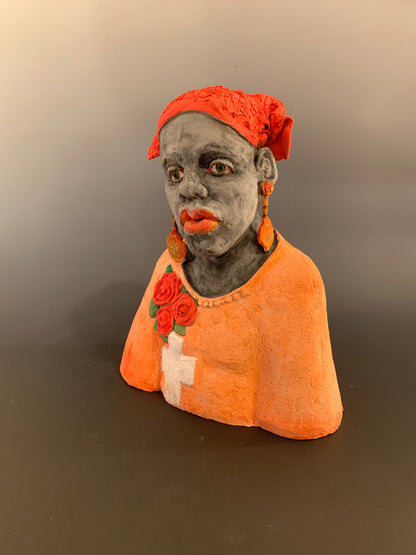 Small figurine of a person wearing an orange hood with floral details on a plain background