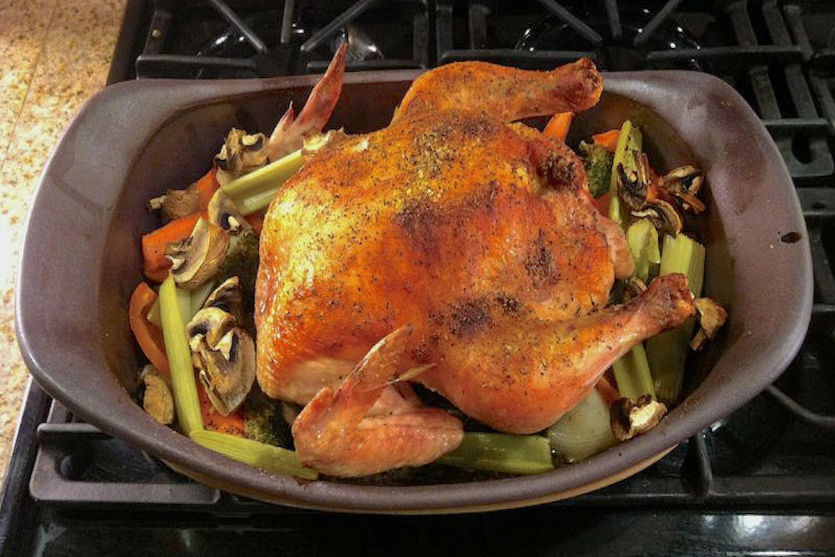 Roasted chicken with vegetables in a baking dish on a stovetop.