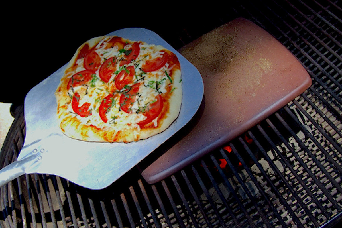 Small pizza on a metal spatula over a grill