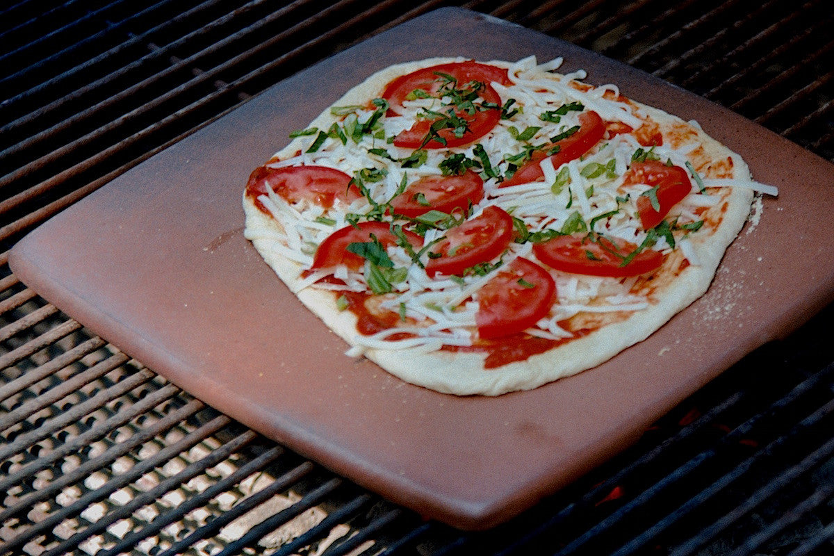 Uncooked pizza with tomatoes and cheese on a grill
