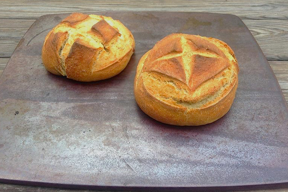 Two loaves of bread on a brown ceramic surface