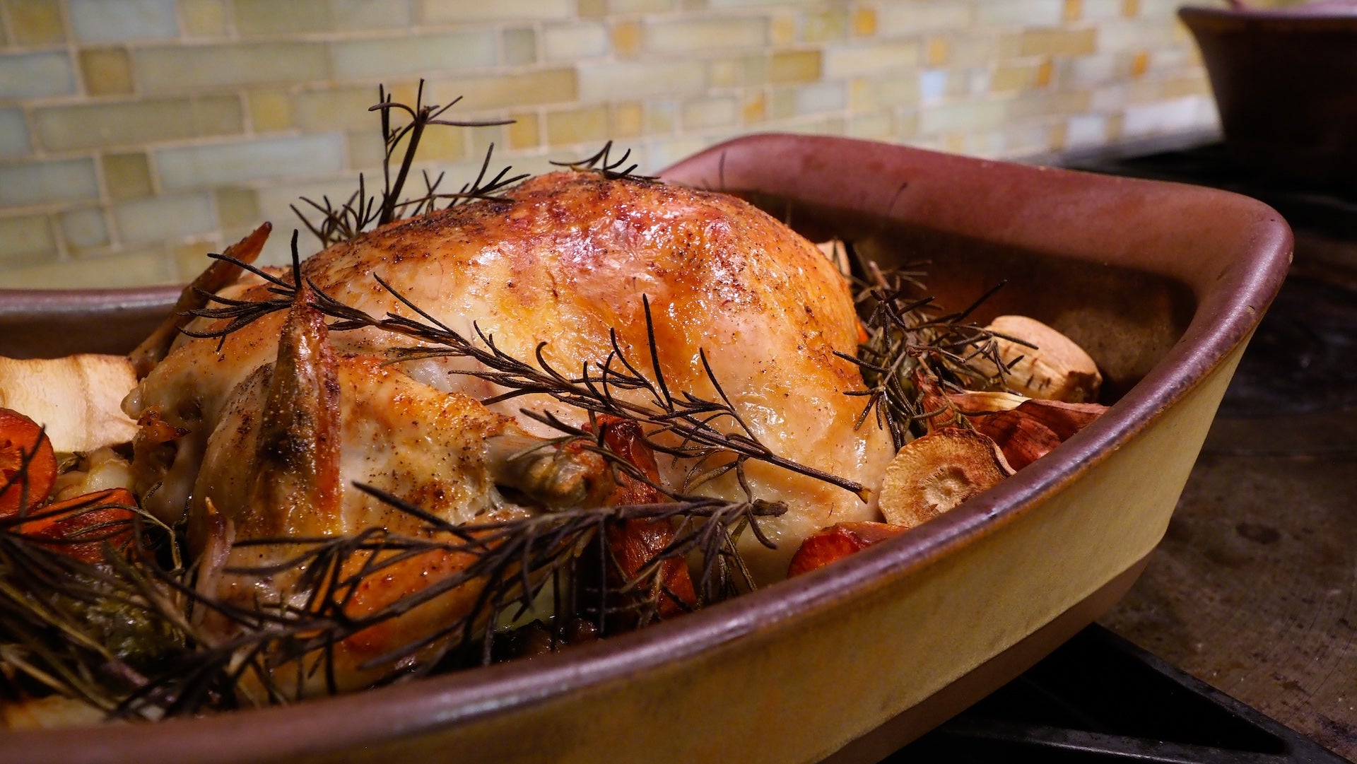 Roasted chicken with herbs in a ceramic dish on a stove