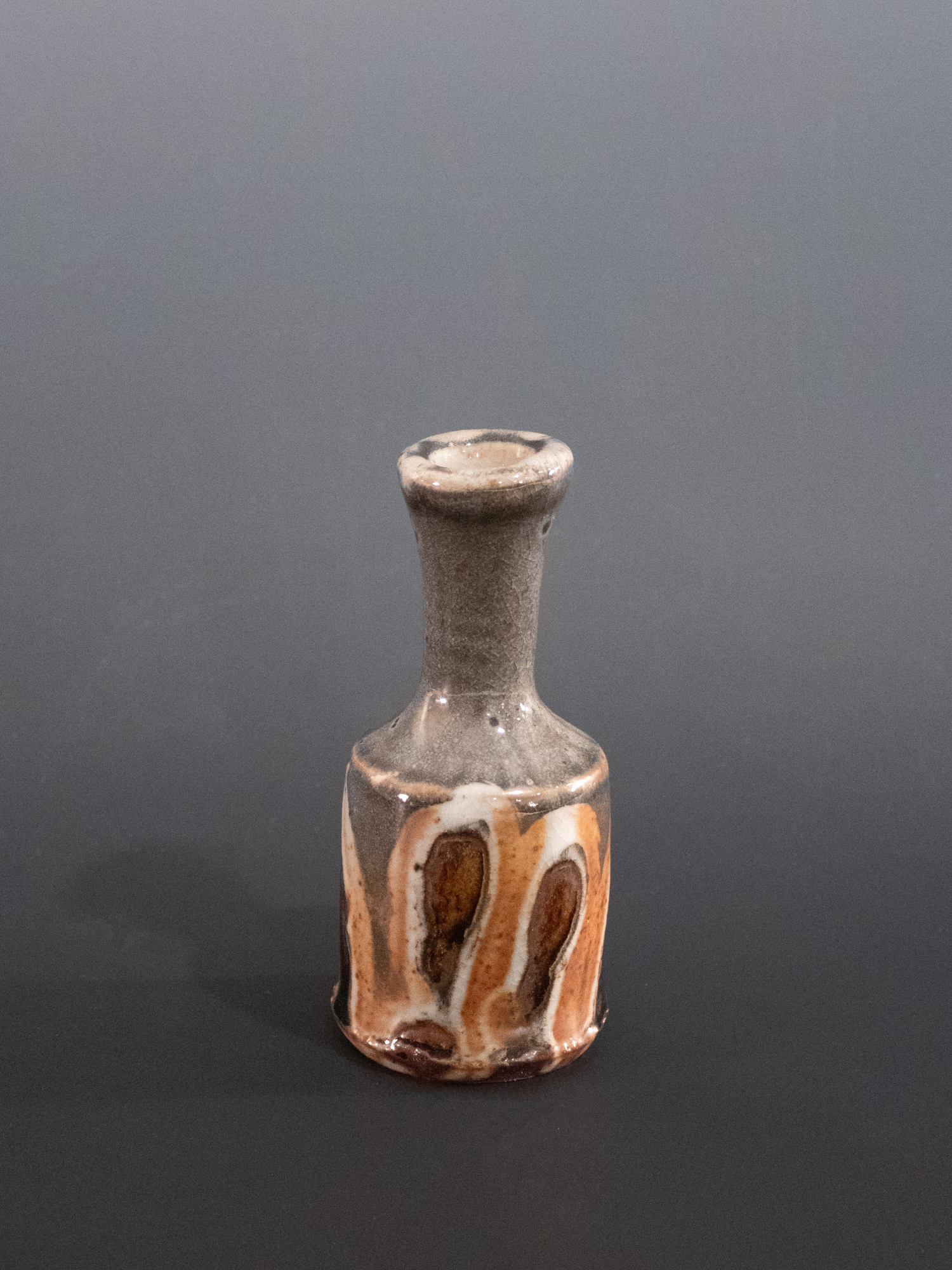 Small ceramic bottle with brown and beige glaze on a gray background