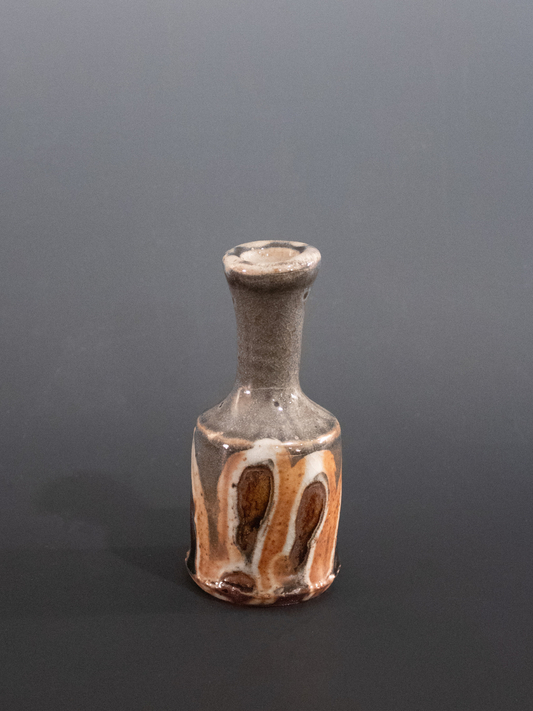 Small ceramic bottle with brown and beige glaze on a gray background