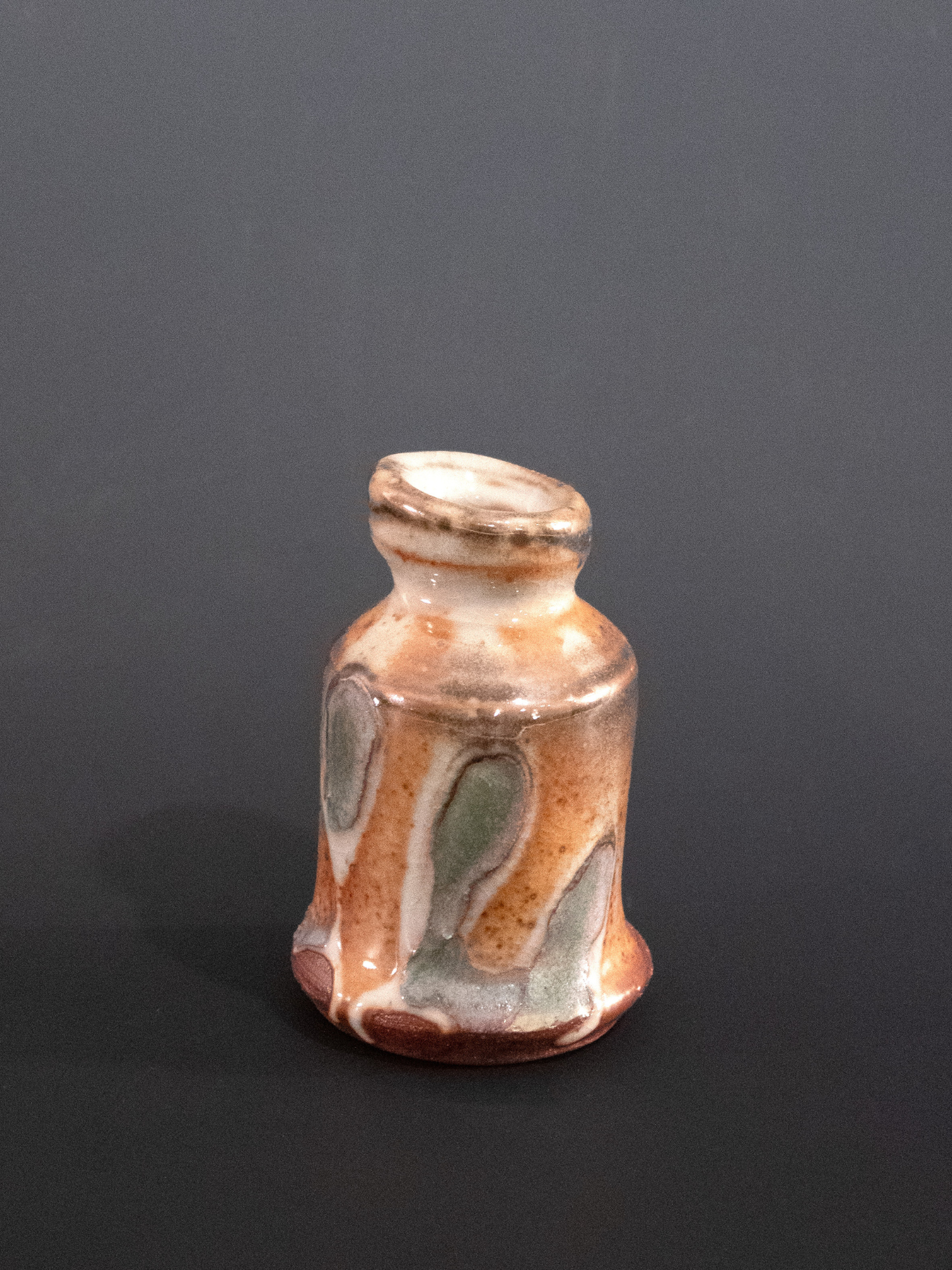 Small ceramic bottle with multicolored glaze on a dark background