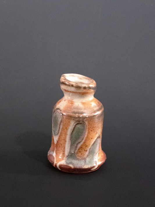 Small ceramic bottle with multicolored glaze on a dark background