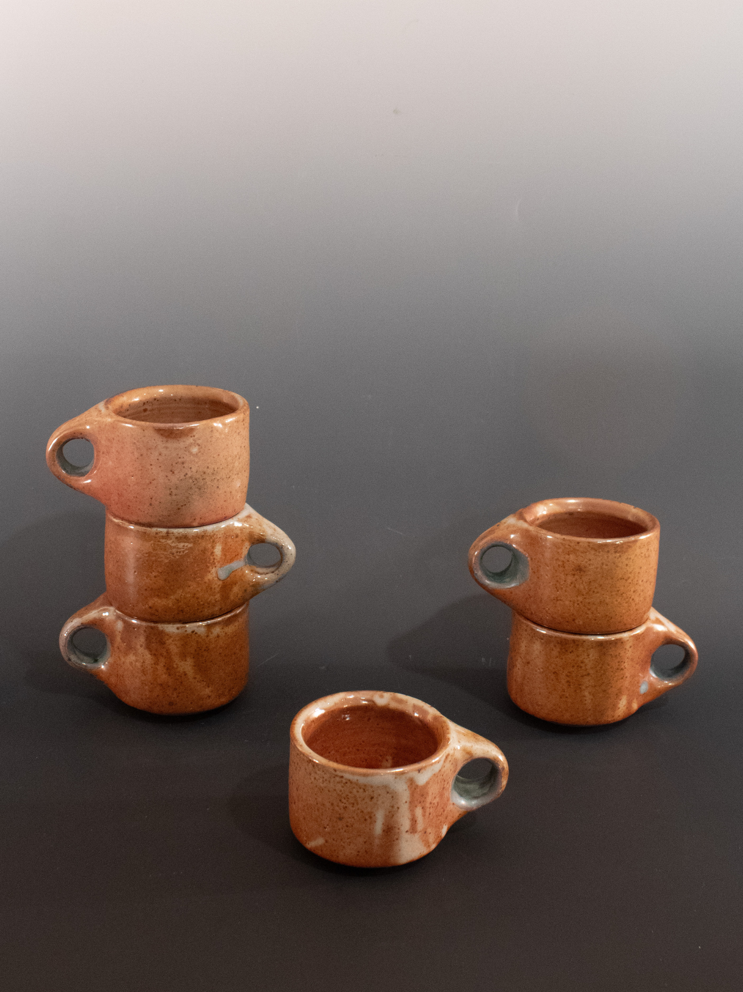 Set of 6 brown ceramic cups with handles on a dark surface.