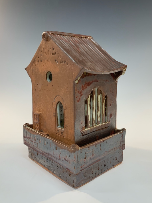 Ceramic model of a small building with a sloped roof on a neutral background