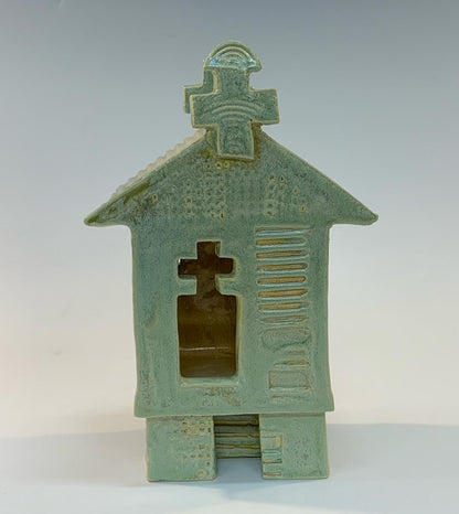 Green ceramic house-shaped object with cross design on a white background