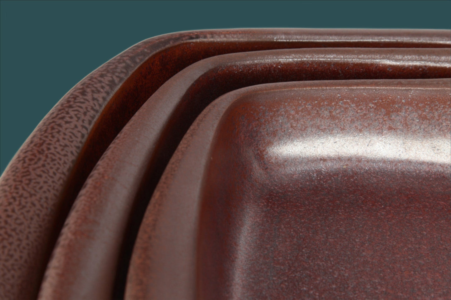 Close-up of a set of brown ceramic trays with a dark green background