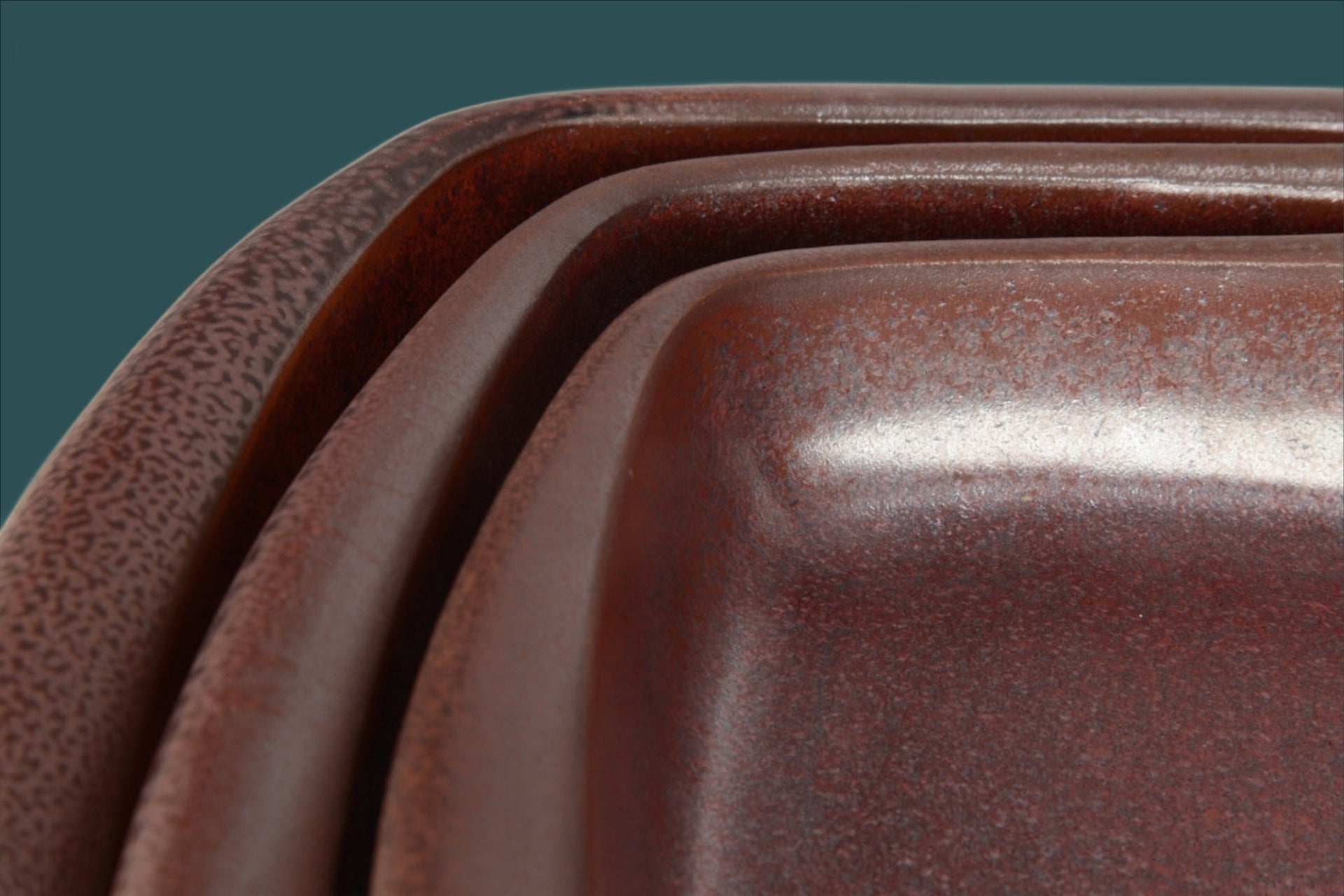 Close-up of a set of brown ceramic trays with a dark green background