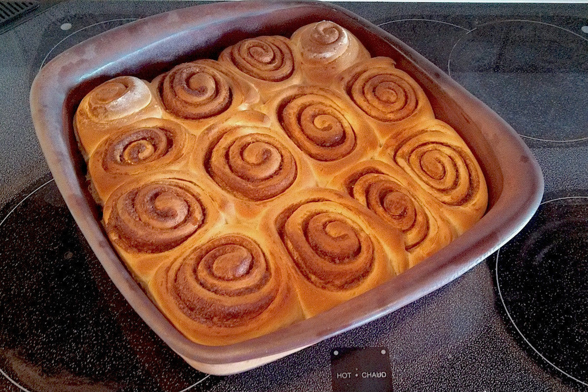 Baked cinnamon rolls in a baking dish on a stovetop.