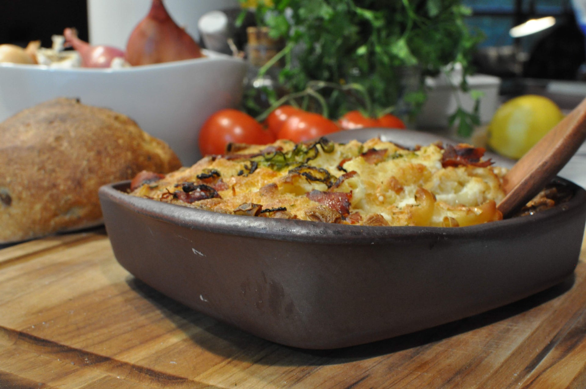 Casserole dish with food on a wooden table with vegetables in the background