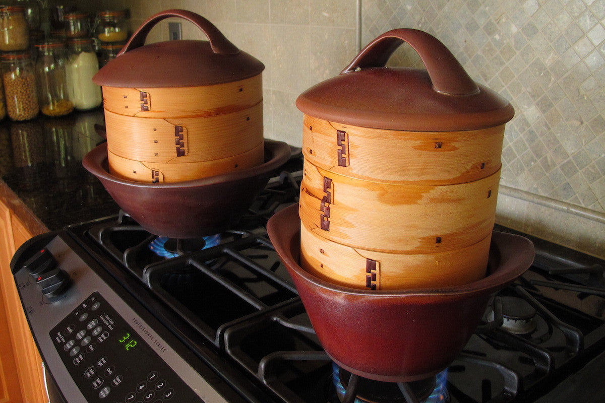 Two wooden steamer baskets with red stands on a stovetop.