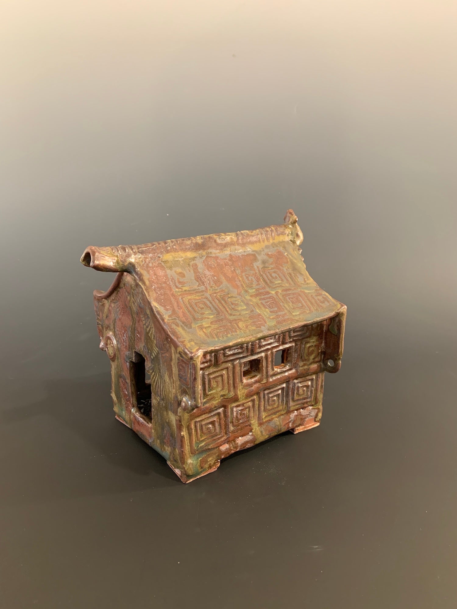 Small ceramic model of a house with geometric patterns on a gray background